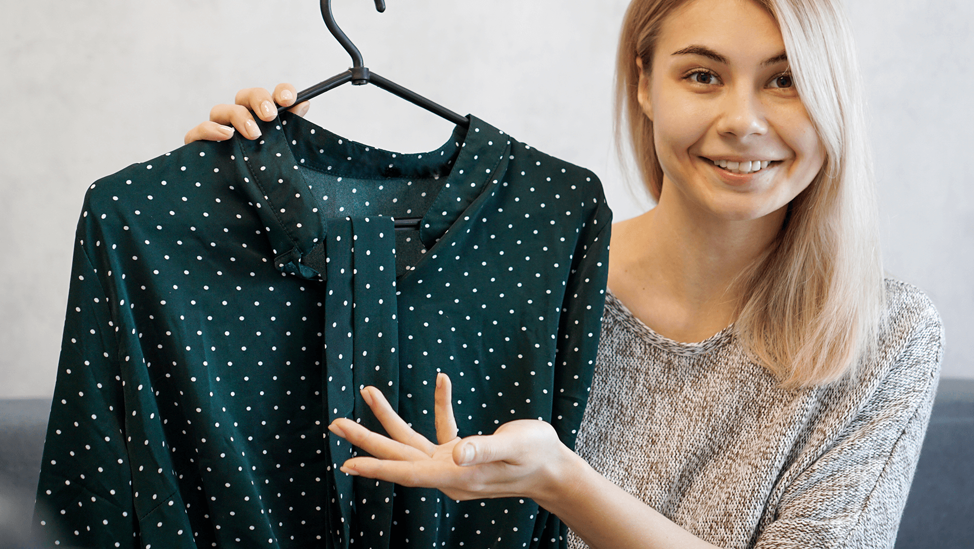A cheerful young woman showcasing a polka-dotted green blouse on a hanger.