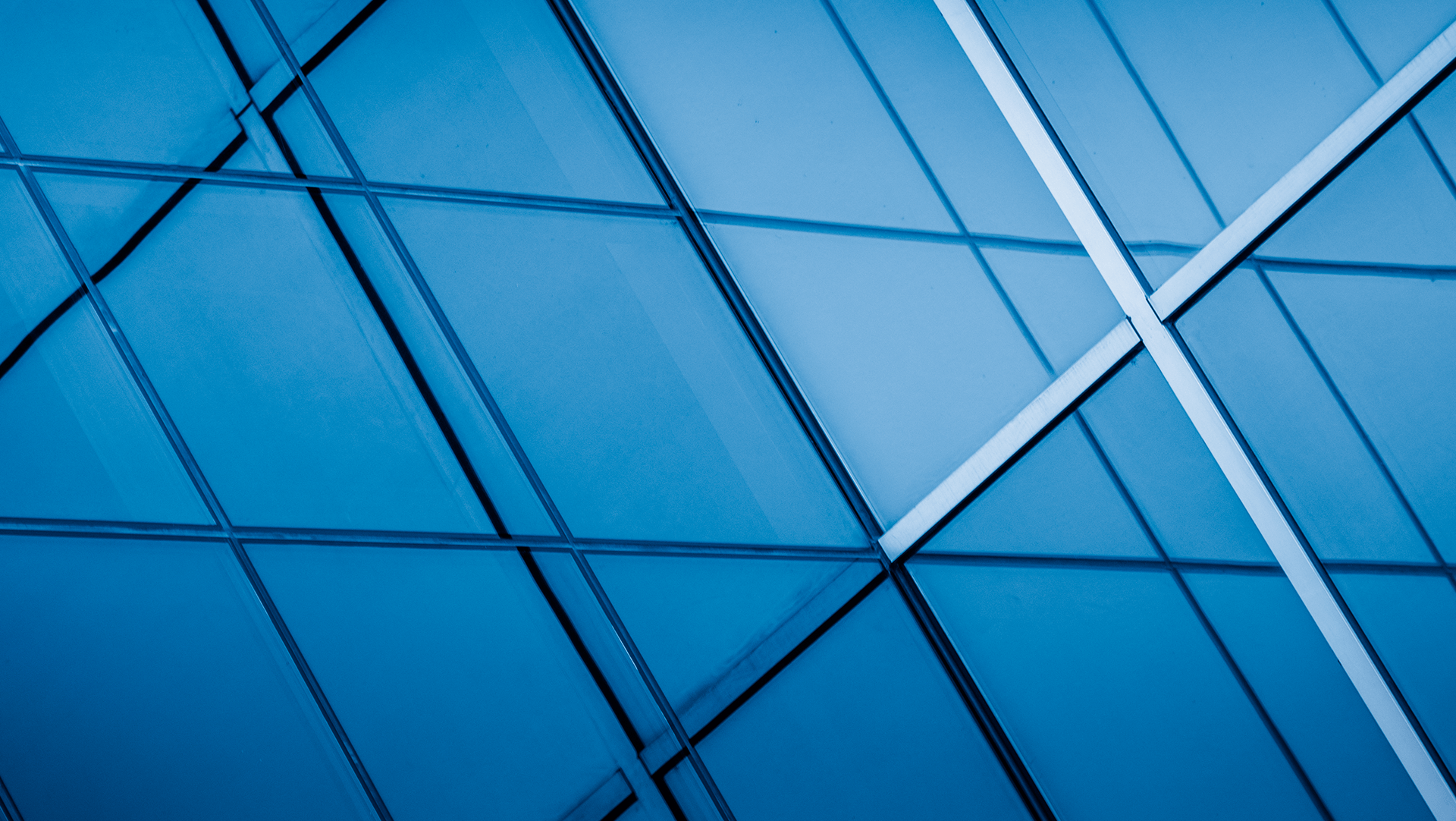 Abstract view of a modern glass building facade with geometric patterns and a cool blue tint.