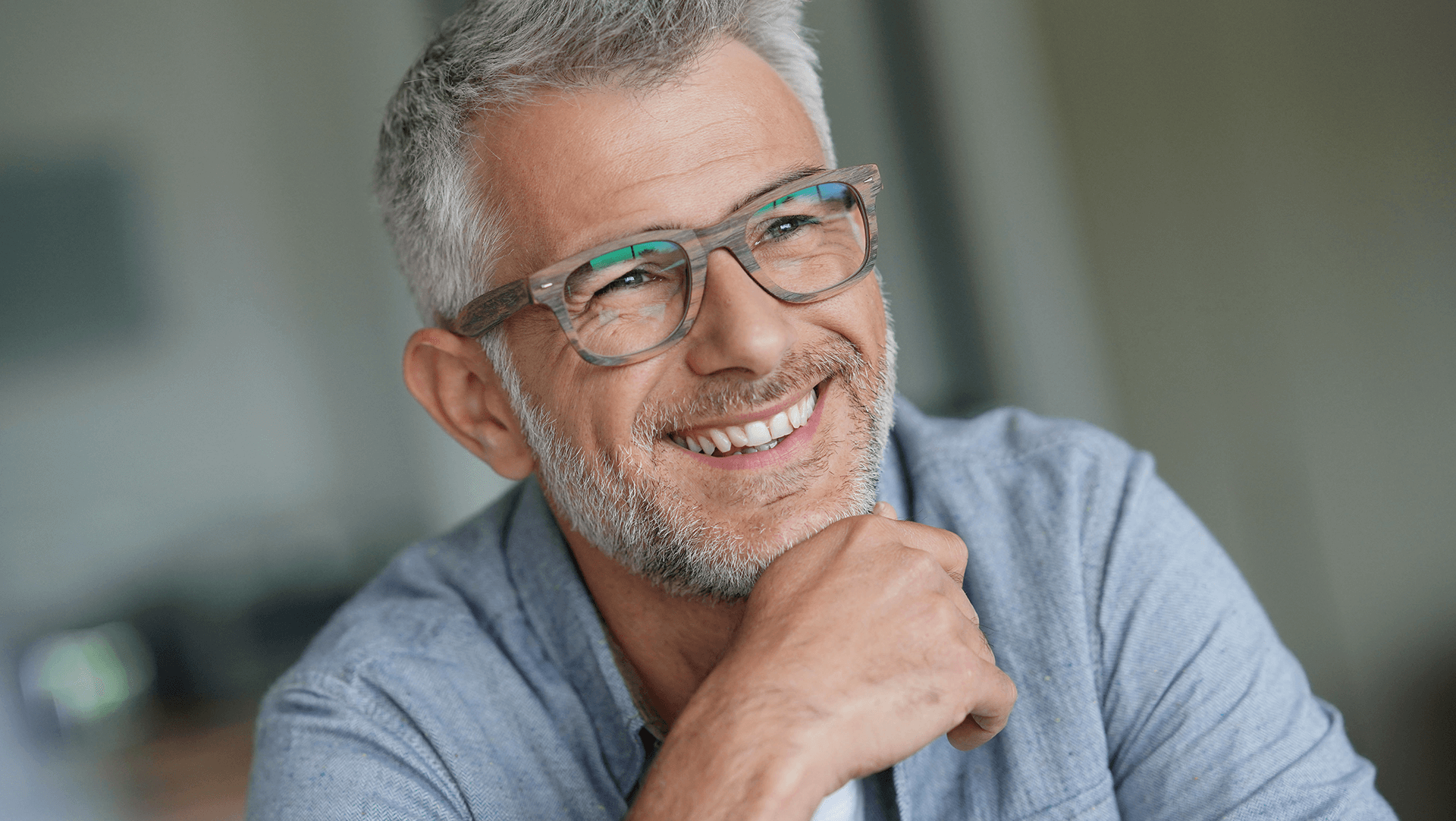 A cheerful mature man with glasses, smiling and looking off into the distance with a look of contentment and optimism.