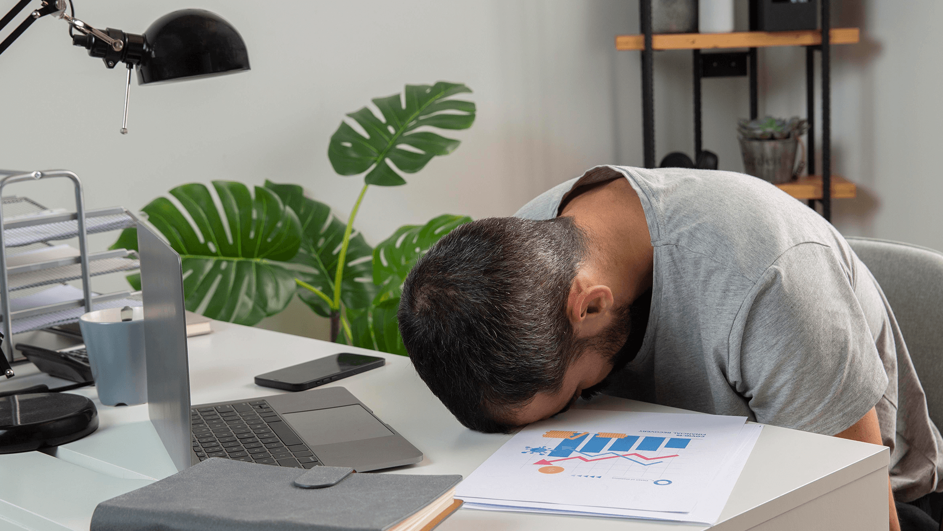 Exhausted office worker asleep on desk with laptop and documents.