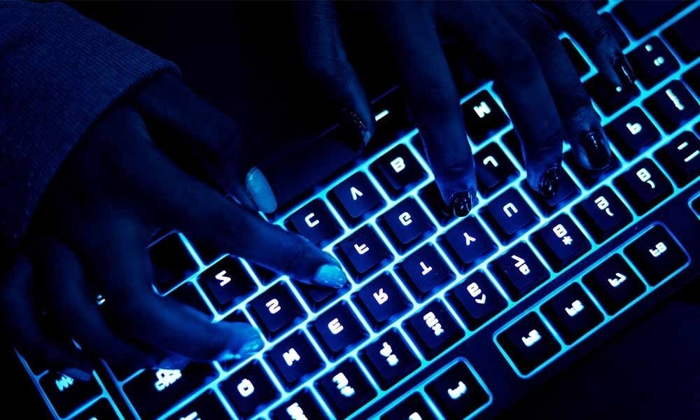 Hands typing on a backlit keyboard in a dimly lit environment, highlighting the interplay of technology and user interaction.