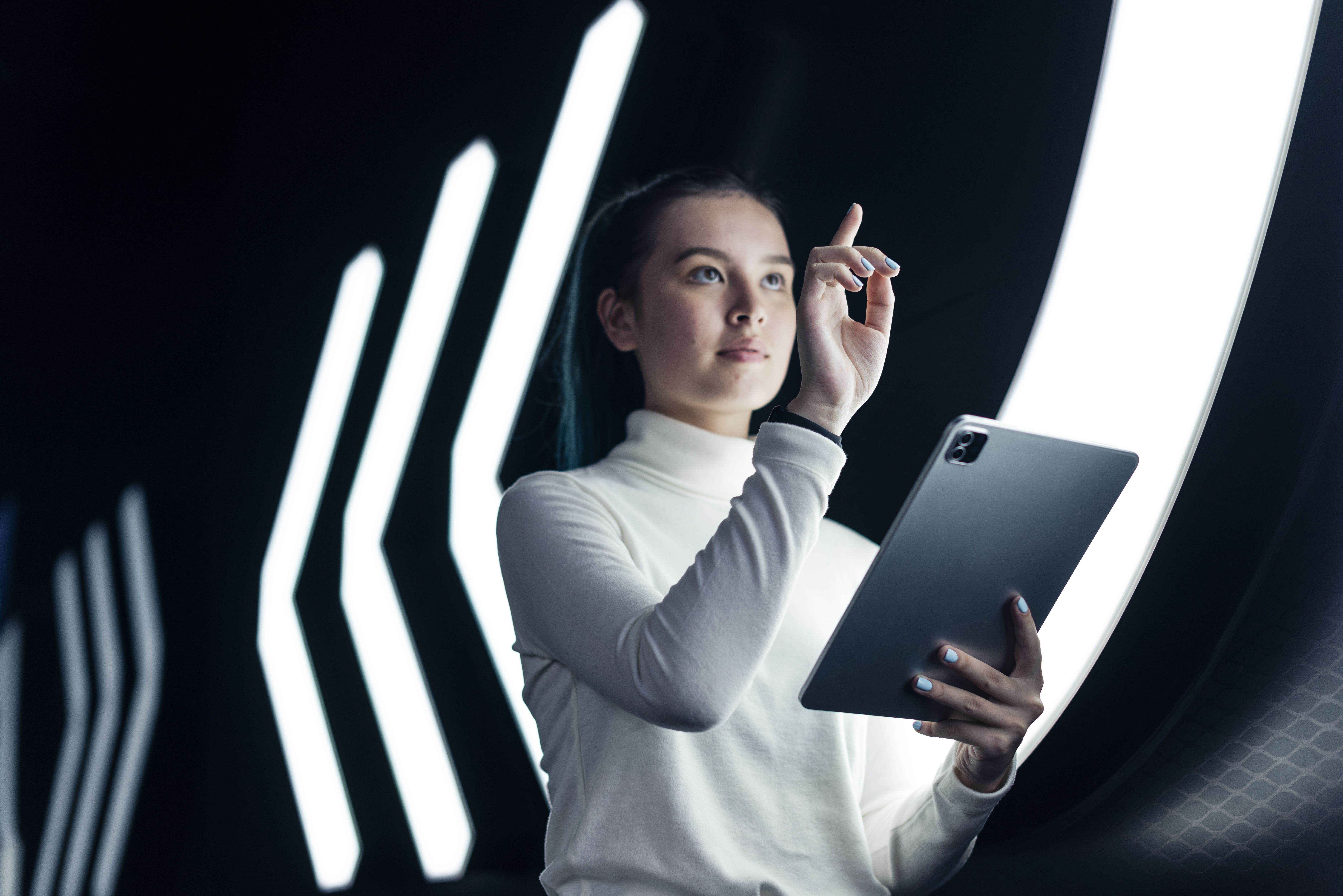 A young woman interacting with a futuristic interface while holding a tablet in a high-tech environment with glowing neon lights.